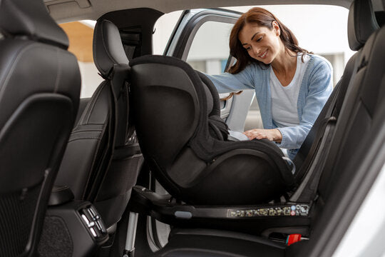 A woman installing a rear-facing convertible car seat in the back seat of a vehicle, reviewing the instruction manual.