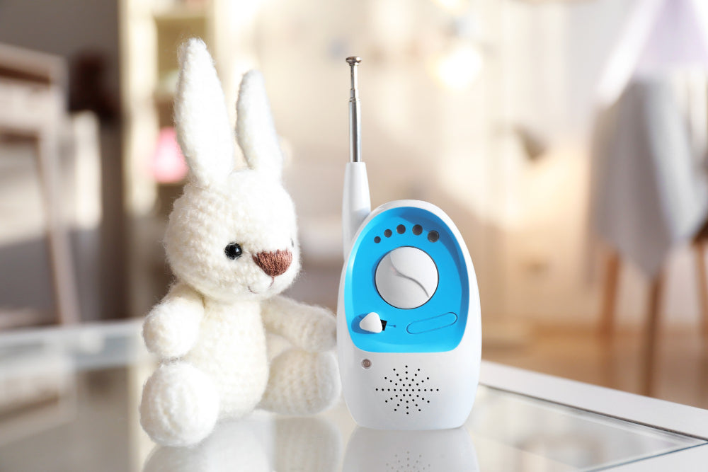 Baby monitor with antenna next to white plush bunny toy on table in softly lit baby nursery.