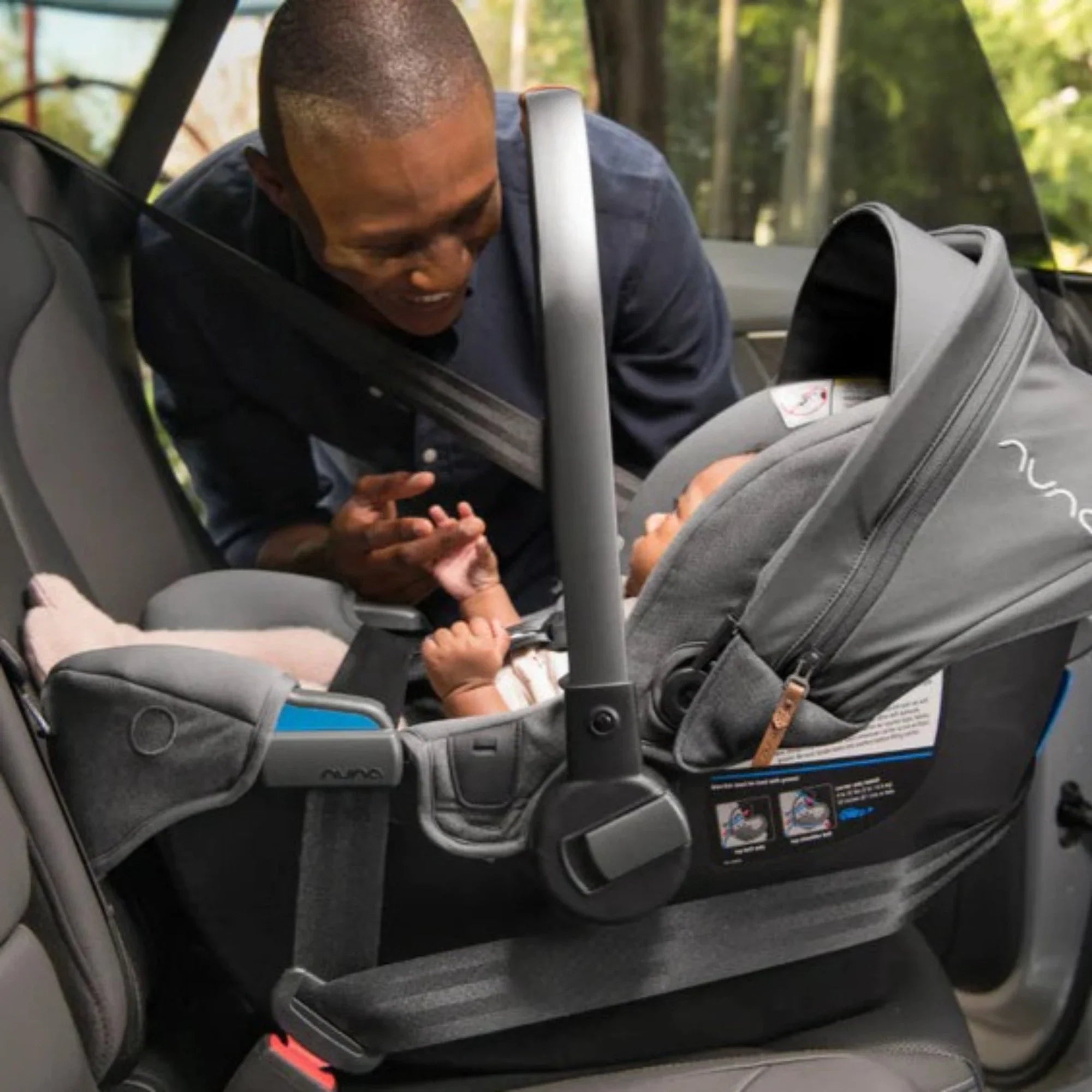Father smiles lovingly as his son sits safely and comfortably in the Nuna PIPA infant car seat, enjoying the ride.