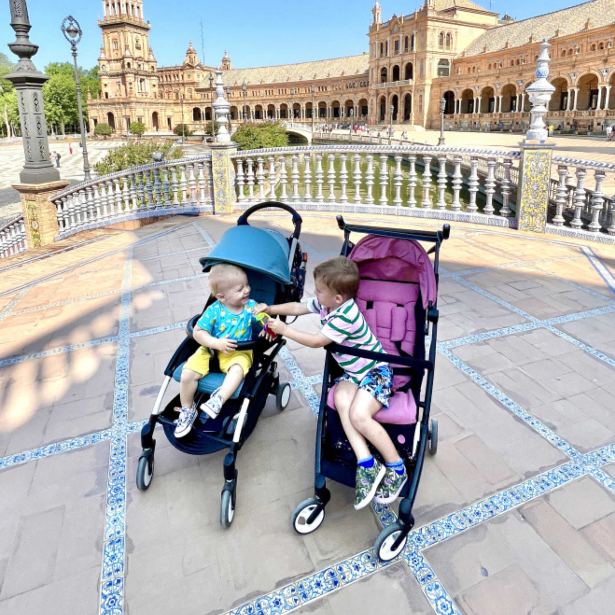Two young children seated in compact strollers at a historic plaza, showing stylish, travel-ready designs often seen when exploring what strollers celebrities use.