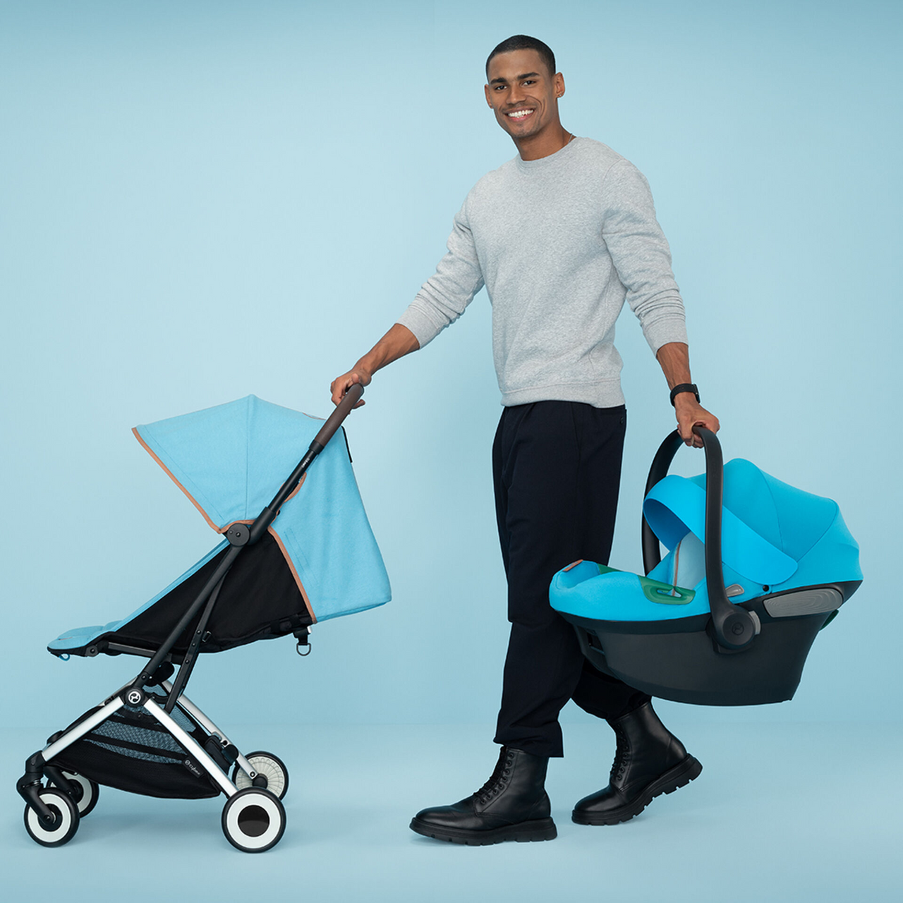 A man holds a CYBEX Orfeo stroller in Beach Blue in one hand and a car seat in the other. 2