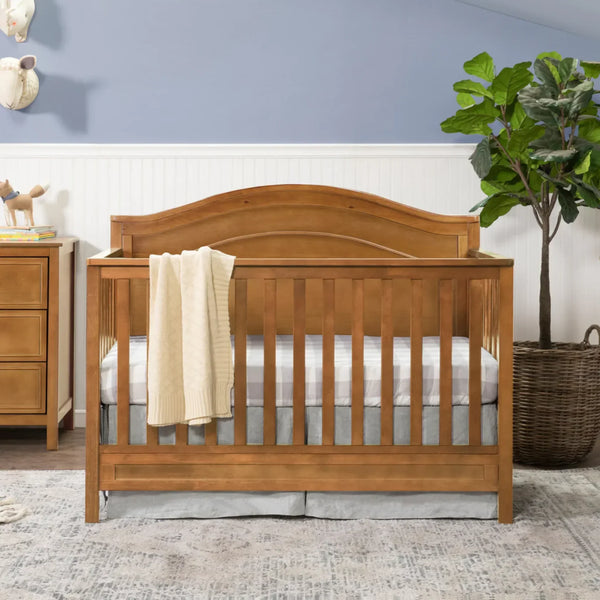 A chestnut-finish convertible crib with a curved headboard in a styled nursery. 