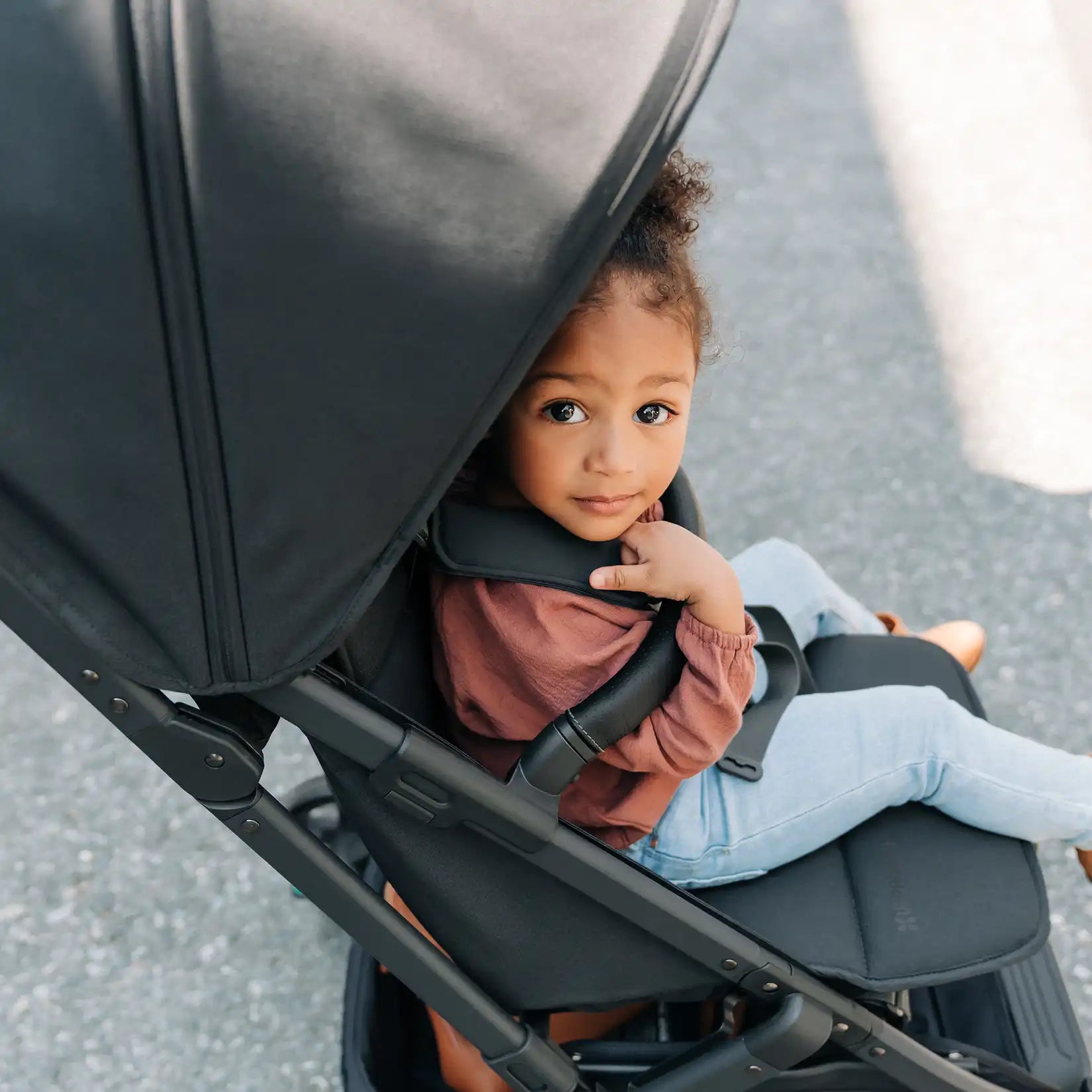 Toddler in UPPAbaby Minu V2 stroller looking up from under canopy on a sunny day.