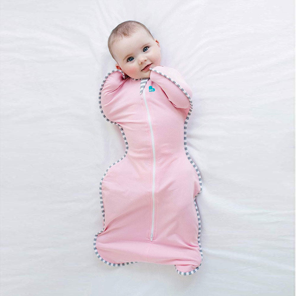 Smiling baby resting comfortably in a soft Love to Dream Swaddle Up, arms up and cozy for calm, happy sleep. 