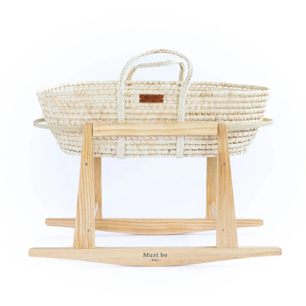 Natural palm-woven Moses basket with braided carry handles resting on a light wood rocking stand, front-facing product shot on white. 
