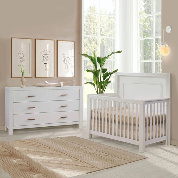 Natart convertible crib in white with panel headboard and slatted sides, displayed in a styled nursery alongside a matching six-drawer dresser.