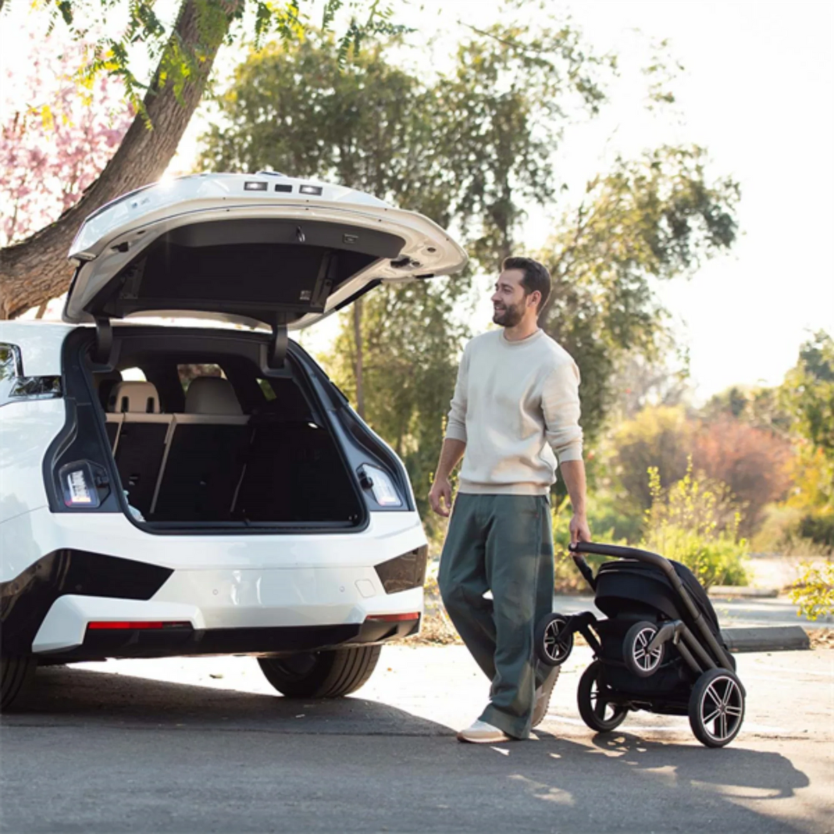 Nuna MIXX Next stroller folded and wheeled toward an open car boot, showing the compact fold and self-standing design. 