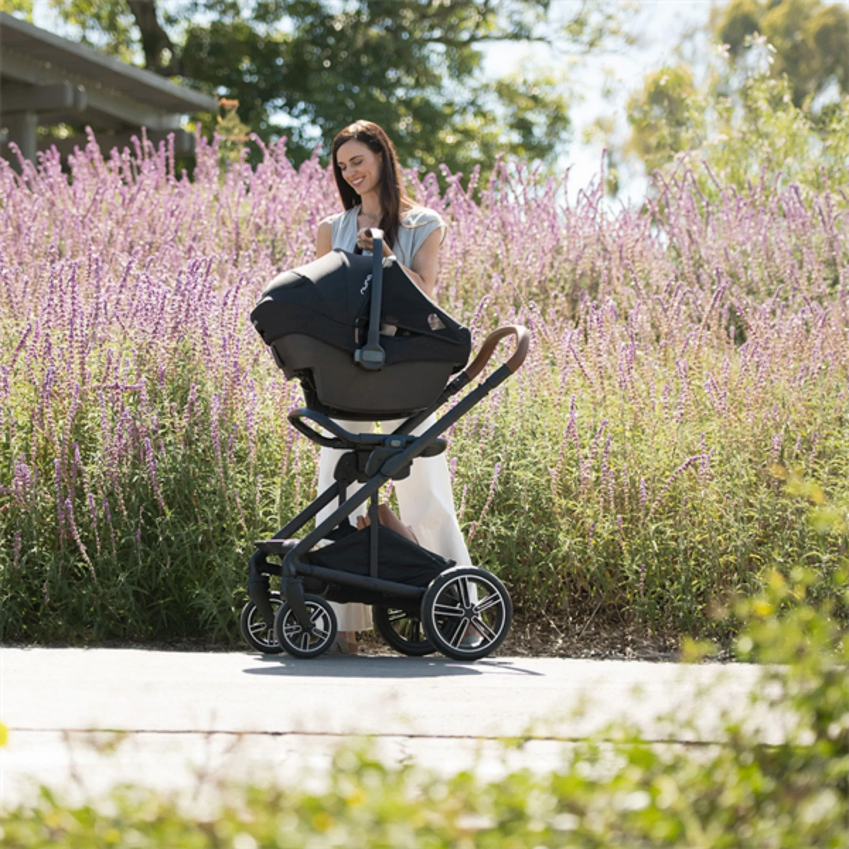 Nuna MIXX Next stroller in travel-system mode with a PIPA infant car seat, parent-facing configuration on an outdoor path. 