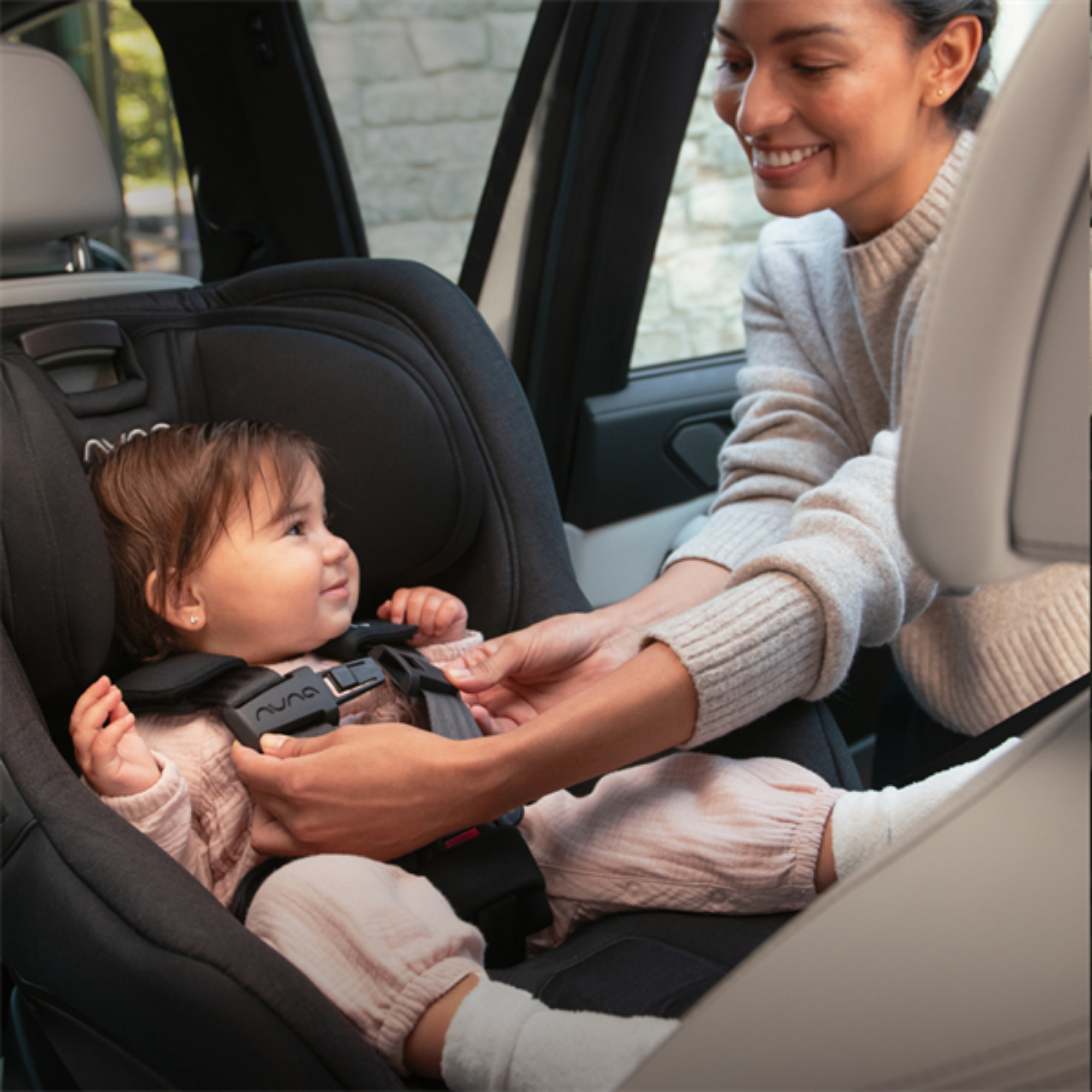 A mom gently secures her baby in the Nuna Rava convertible car seat, ready for a safe and comfortable forward-facing ride. 