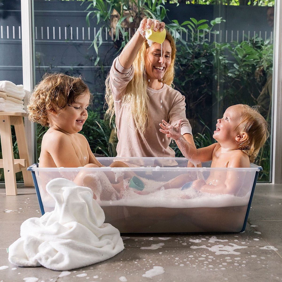 Two kids laughing in the Stokke Flexi Bath while mom stands nearby, making bath time safe, easy, and fun.