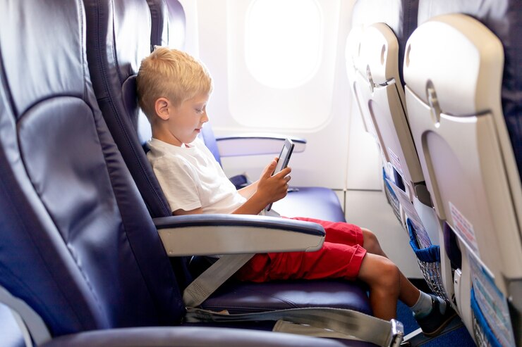 Young boy sitting on an airplane seat, using a tablet during flight.