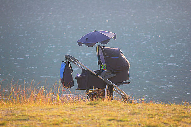 Dark navy pram parked outdoors by a lake, with a stroller sunshade/parasol attached