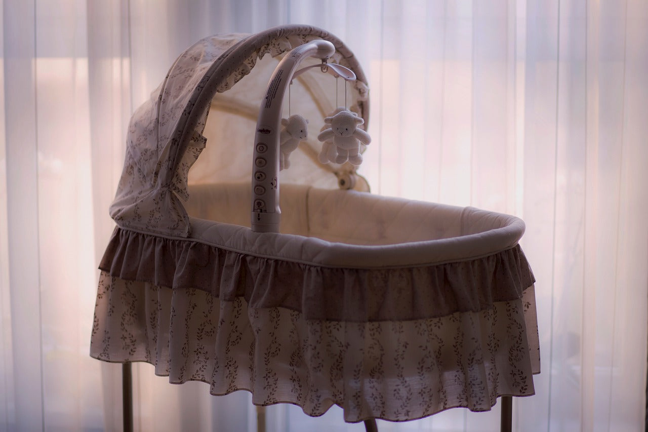 A traditional baby bassinet with a canopy and mobile white fabric nursery.