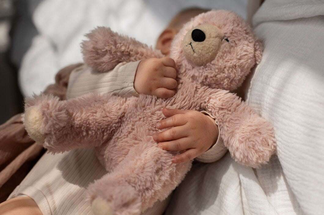 Baby cuddling a soft, fluffy light brown teddy bear while resting on a cozy white blanket.