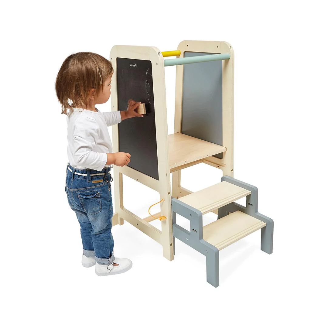 Toddler using Janod wooden learning tower with chalkboard panel and steps, designed for safe elevated standing and creative play.