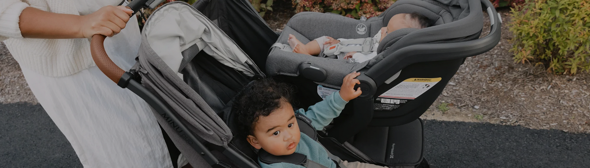 Parent pushing a stroller with a toddler looking out from the seat, a family scene for double strollers with car seat compatibility.