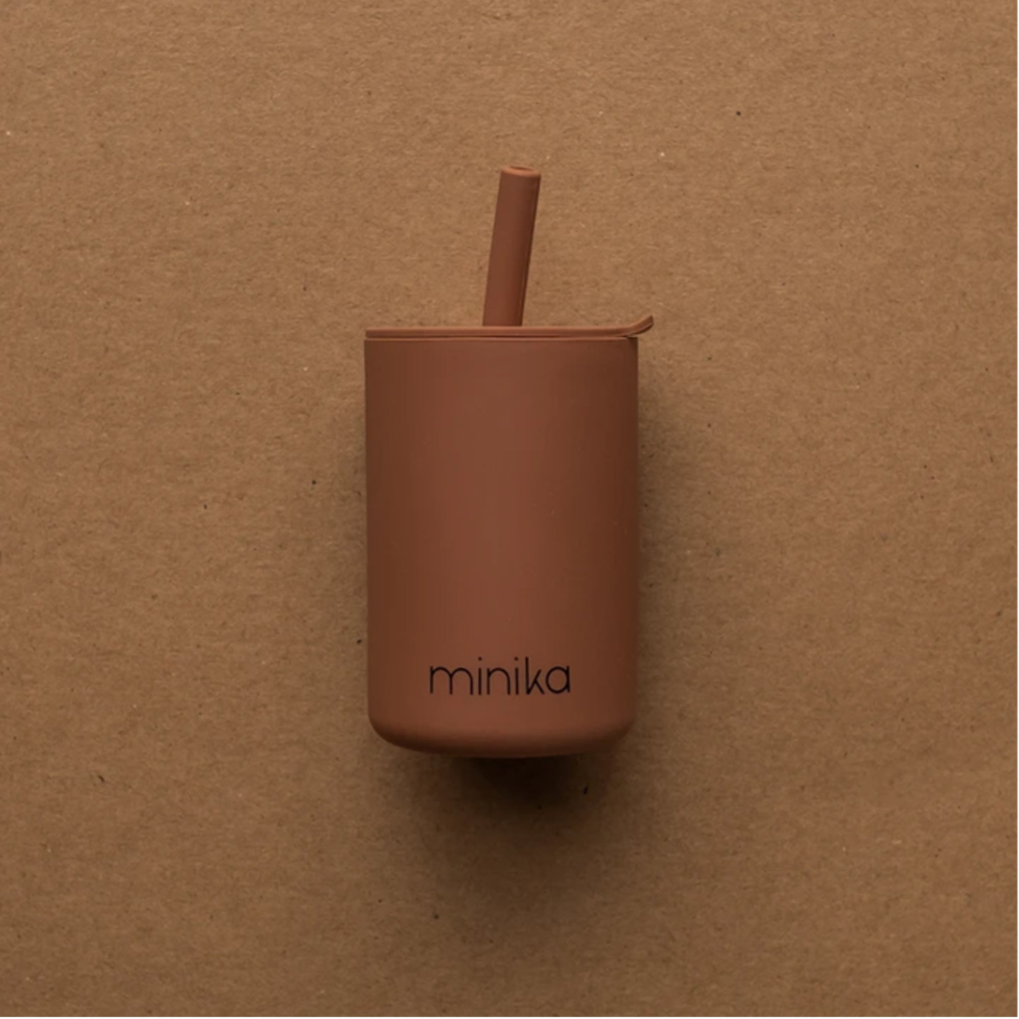 Terracotta silicone training cup with built-in straw and “minika” logo, designed for babies learning to drink independently.